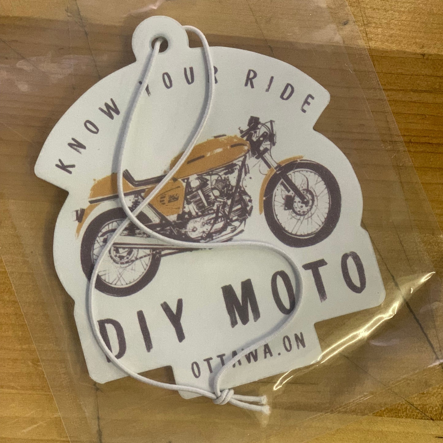 One motorcycle-themed air freshener in a clear plastic bag on a wooden surface.