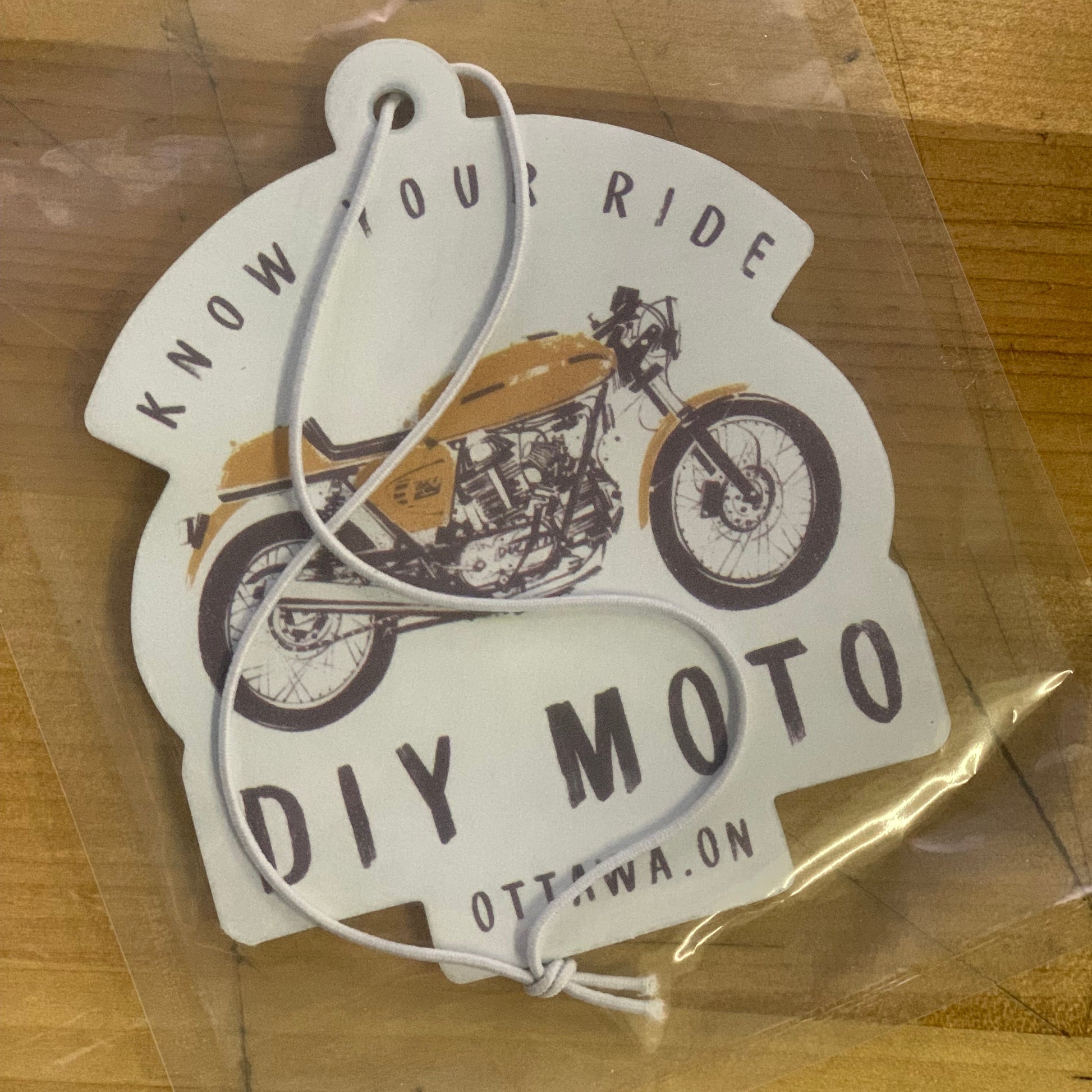 One motorcycle-themed air freshener in a clear plastic bag on a wooden surface.